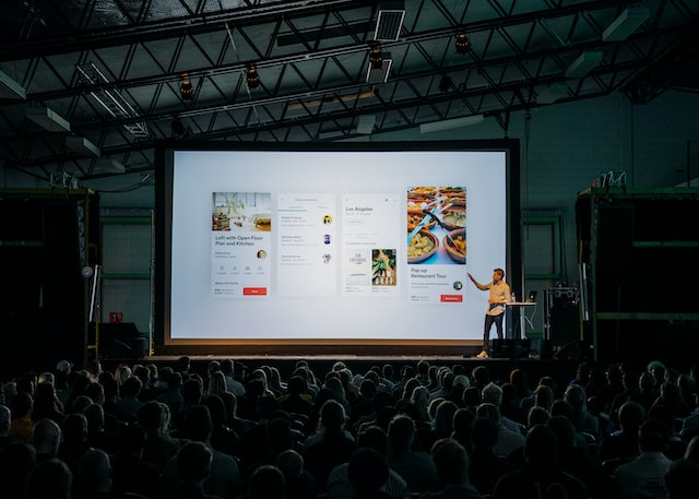 person discussing while standing in front of a large screen