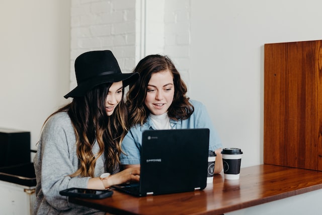 two woman sitting near table using laptop